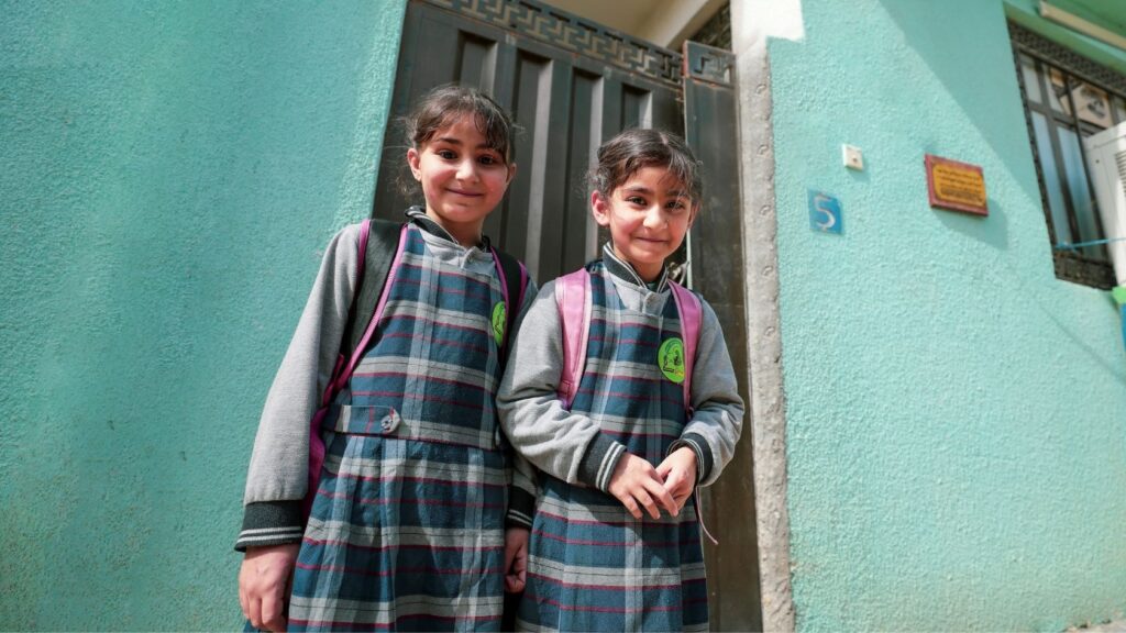 Deux jeunes écolières en uniforme, cartable sur le dos, devant la porte de leur maison