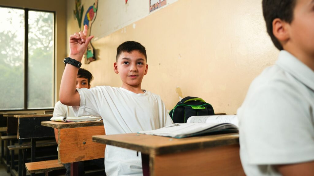 Un élève assis à son pupitre lève la main pour répondre en classe