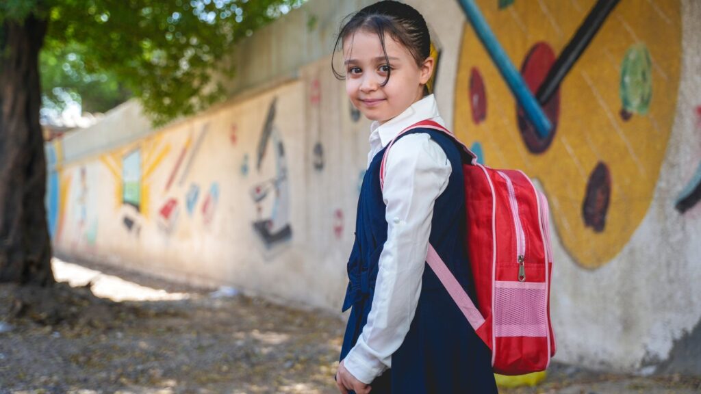 Une écolière en uniforme portant un cartable rouge sur le chemin de l’école